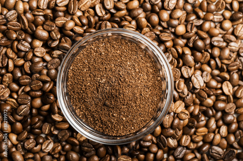 Natural ground coffee heap in transparent glass bowl on сoffee grains background