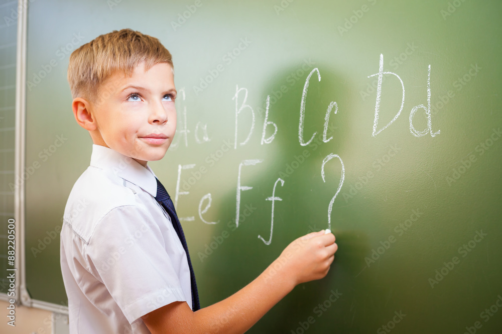 School boy writes English alphabet with chalk on blackboard School boy writes English alphabet with chalk on blackboard