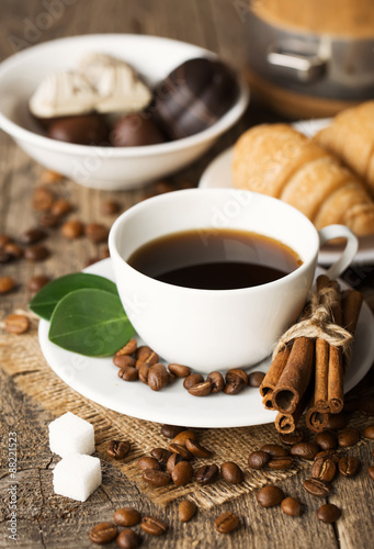 Close-up of coffee cup with roasted coffee beans on wooden background.