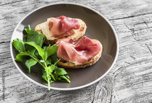 toast with ham and fresh arugula on a brown plate on a light wooden background