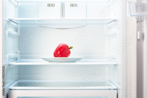 Red pepper on white plate in open empty refrigerator