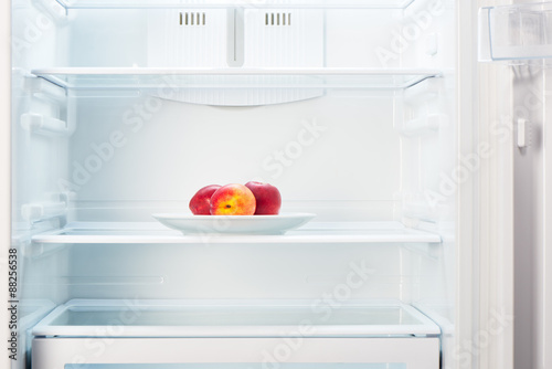 Peaches on white plate in open empty refrigerator