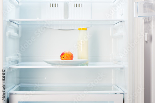 Peach on white plate with bottle of yogurt in refrigerator