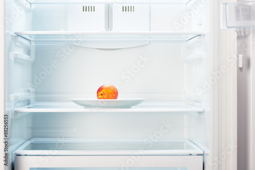 Peach on white plate in open empty refrigerator