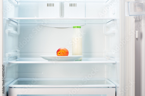 Peach on white plate with bottle of yogurt in refrigerator