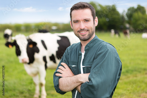 Fototapet Portrait of a young attractive farmer in a pasture with cows