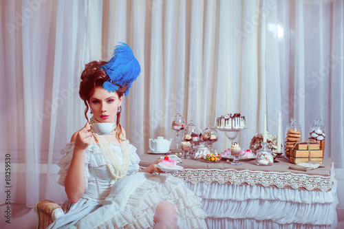Indoors shot in the Marie Antoinette style. Woman drinking tea with sweets.