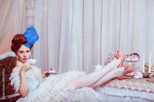Indoors shot in the Marie Antoinette style. Woman drinking tea with sweets. photo