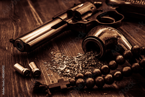 Revolver and a rosary with cross and tobacco pipe on a wooden table
