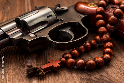 Revolver and a rosary on the wooden table