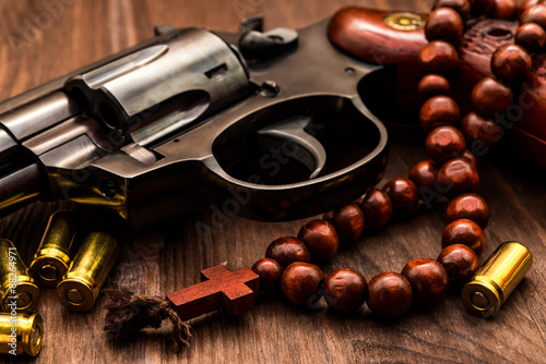 Revolver with cartridges and a rosary on the wooden table