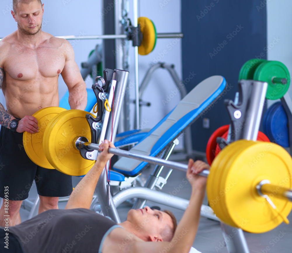 Fototapeta premium Young man lifting the barbell in gym with instructor