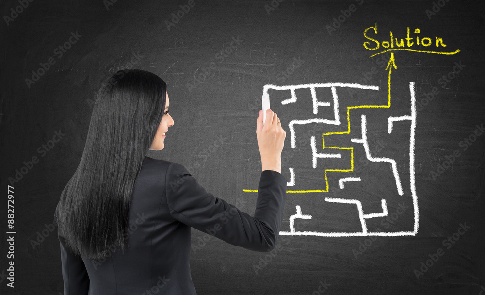 Brunette business woman is drawing a labyrinth with solution on the chalk blackboard. Brunette business woman is drawing a labyrinth with solution on the chalk blackboard.