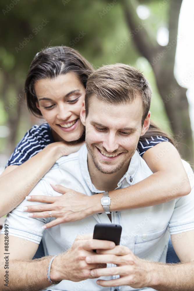 Happy couple watching a smart phone sitting on a bench in a park Happy couple watching a smart phone sitting on a bench in a park