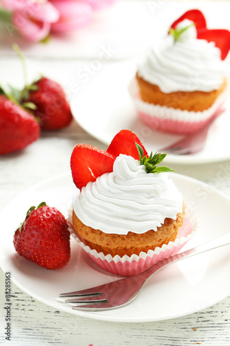 Tasty cupcake with fresh strawberry on white wooden background