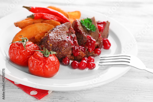 Tasty roasted meat with cranberry sauce and roasted vegetables on plate, on color wooden background