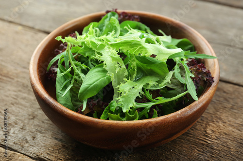 Bowl of mixed green salad on wooden table, closeup