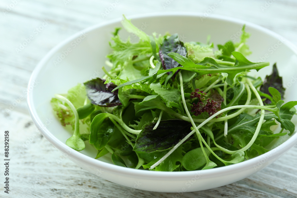 Fresh mixed green salad in bowl on wooden table close up Fresh mixed green salad in bowl on wooden table close up