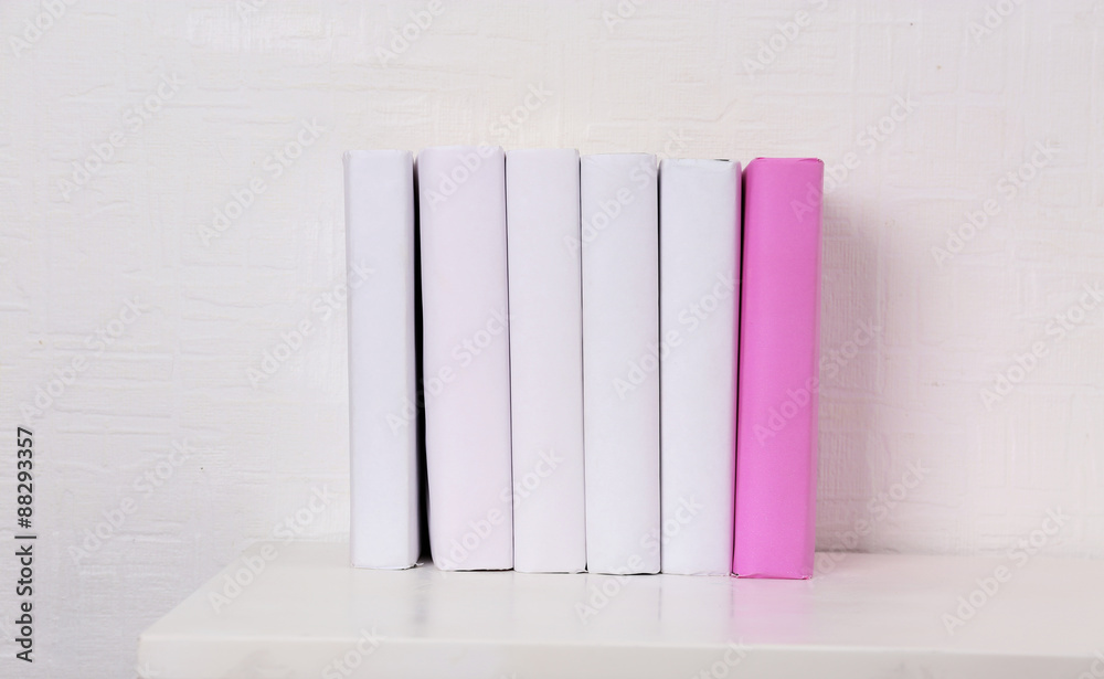 Naklejka premium Blank books and pink one on shelf on white wallpaper background