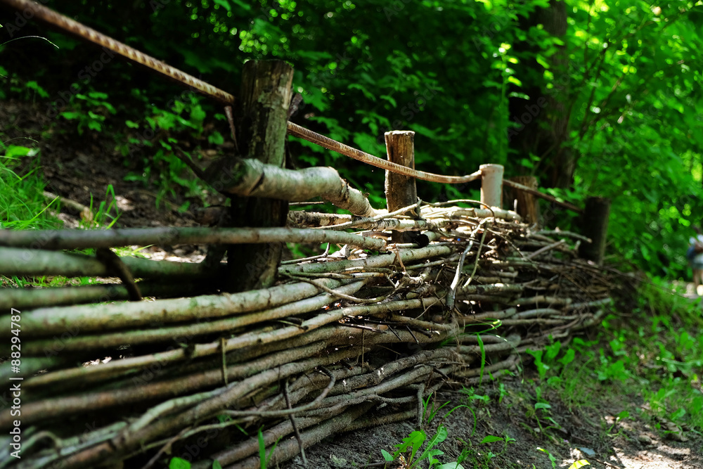 Wooden wicker fence over green trees background Wooden wicker fence over green trees background