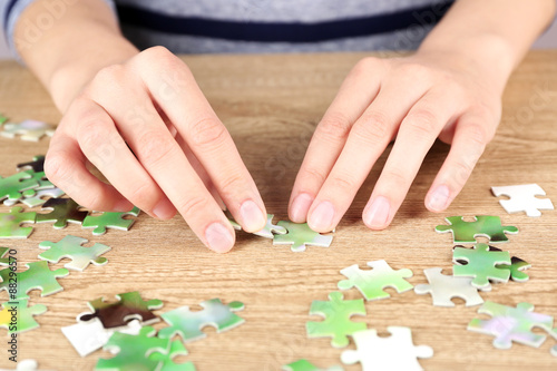 Female hands assembling puzzle on wooden table, closeup