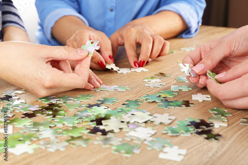 Female hands assembling puzzle on wooden table, closeup