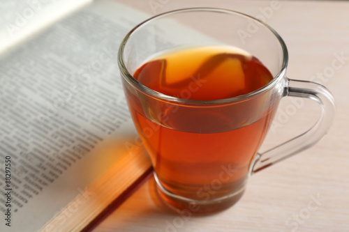 Glass cup of tea with open book on wooden table, closeup