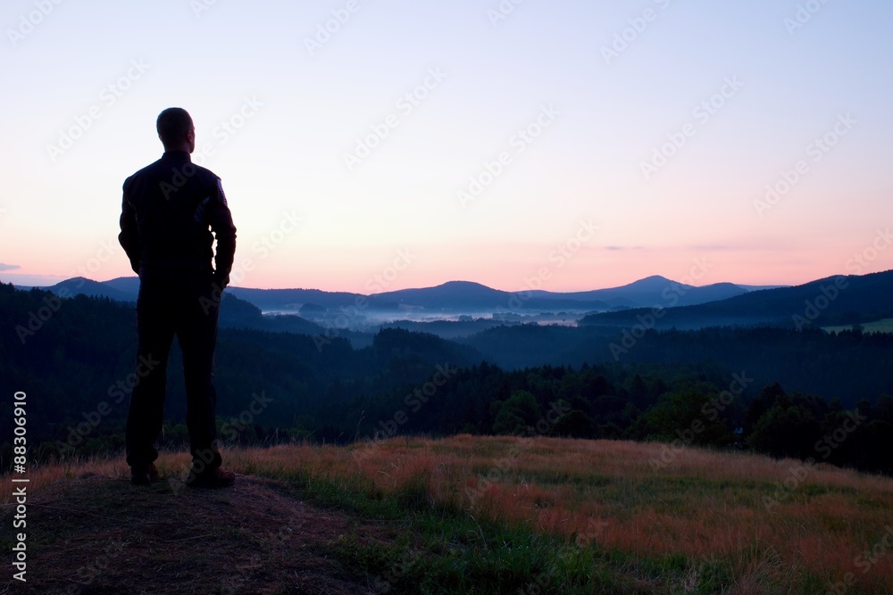 Hiker stand on meadow with golden stalks of grass and watch over the misty and foggy morning valley to sunrise