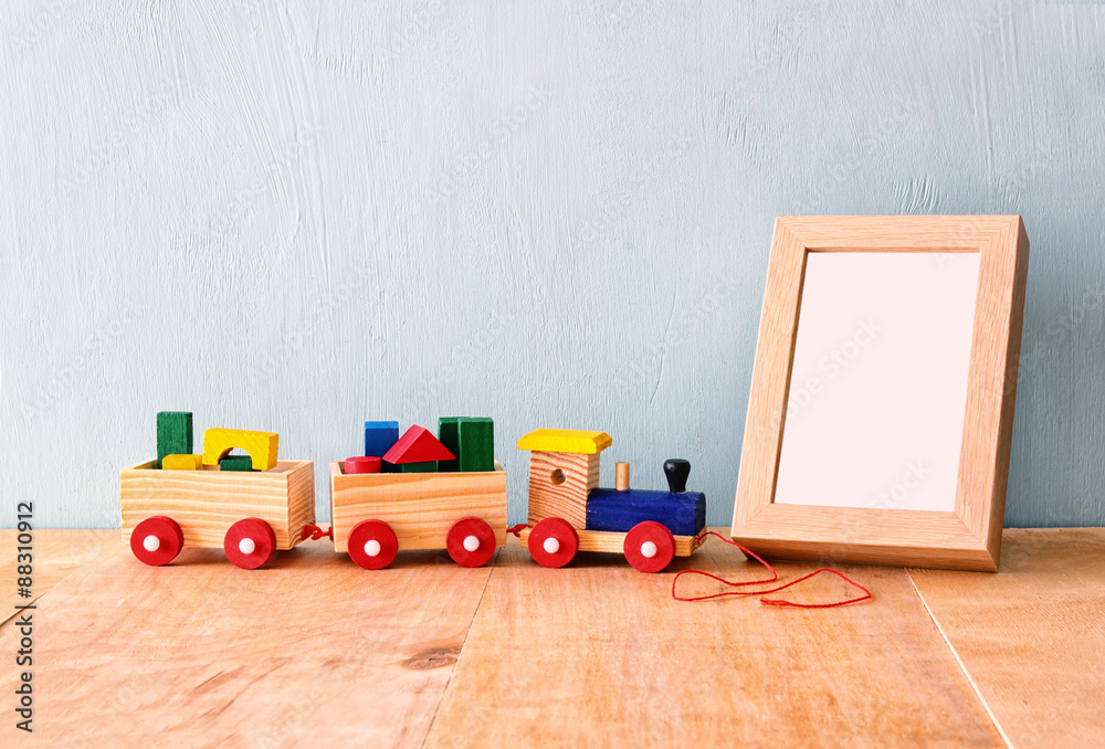 Wooden toy train over wooden table next to photo blank frame Wooden toy train over wooden table next to photo blank frame