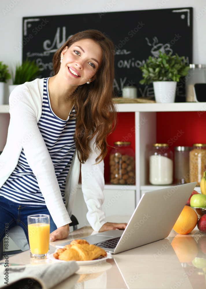 Attractive young woman using laptop and sitting in the kitchen Attractive young woman using laptop and sitting in the kitchen