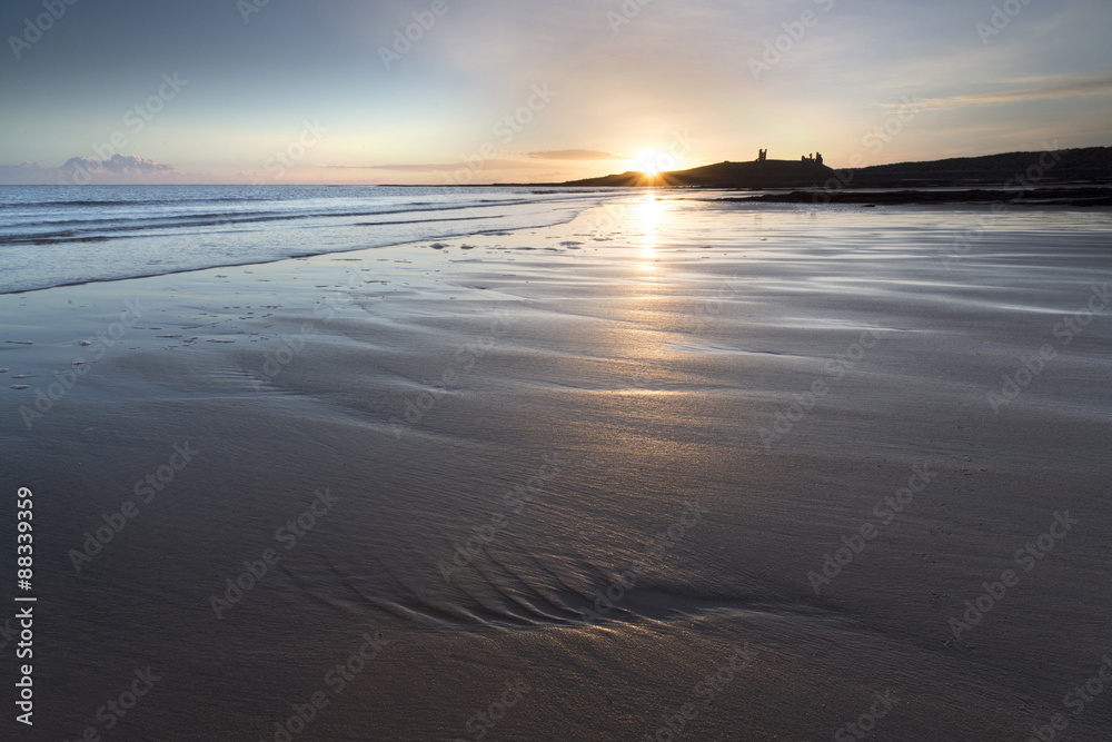 View over Embleton Beach at sunrise towards the silhouetted ruin of Dunstanburgh Castle in the distance, Embleton Bay, near Alnwick, Northumberland View over Embleton Beach at sunrise towards the silhouetted ruin of Dunstanburgh Castle in the distance, Embleton Bay, near Alnwick, Northumberland