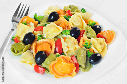 Salad made with tortellini, olives, broccoli, red pepper, on a plate with fork, white background