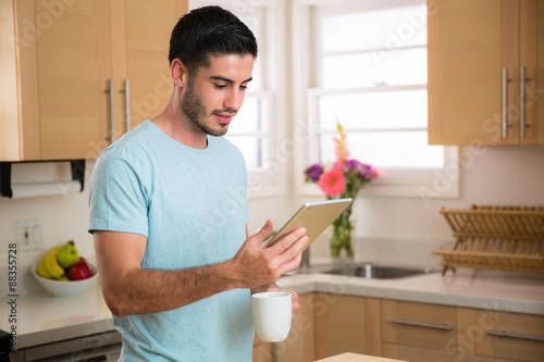 Male reading news on tablet from home kitchen with cup of coffee bright room smart technology device