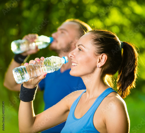 Man and woman drinking water from bottle after fitness sport