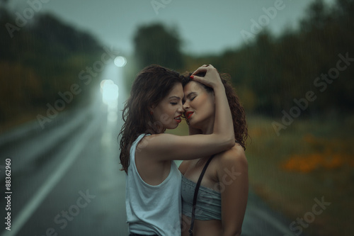 Girls stand having embraced on street in the rain.