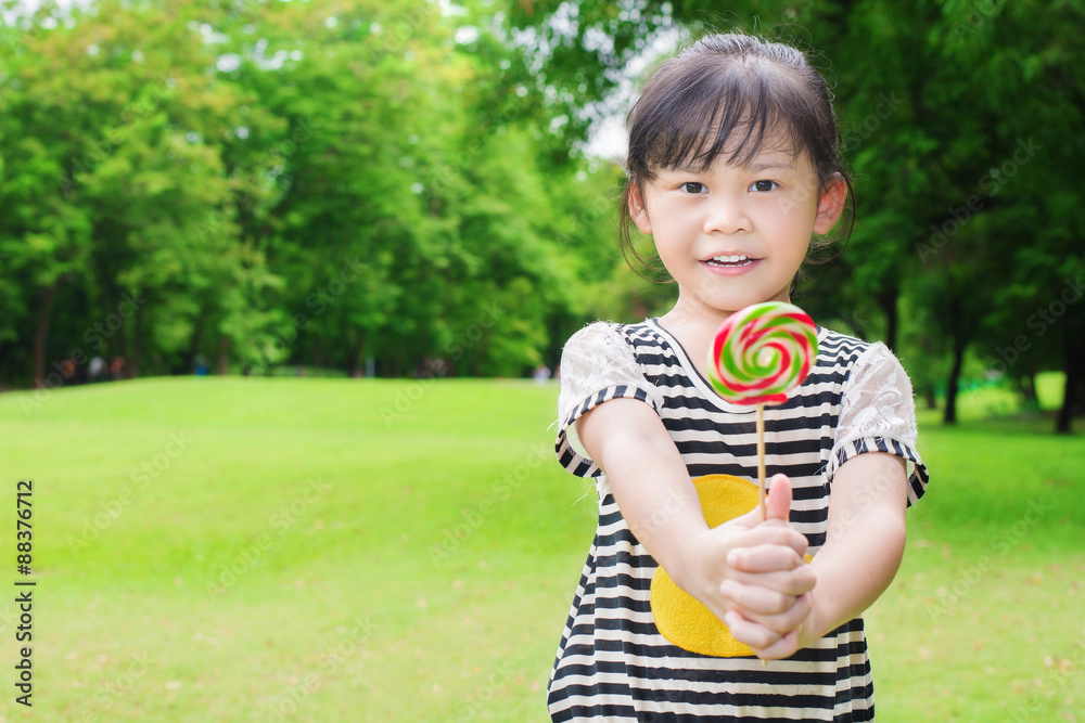 Asian little girl eating lollipop outdoors in spring park Asian little girl eating lollipop outdoors in spring park