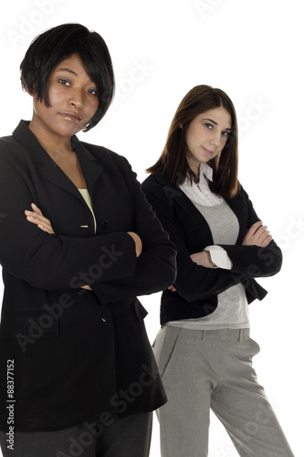 Two women standing with arms crossed. Focus is on woman in front.