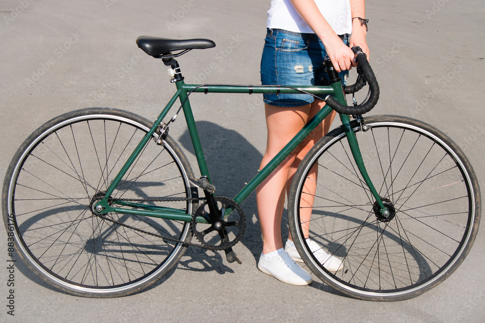 Naklejka premium young woman standing on the road next to a green bike