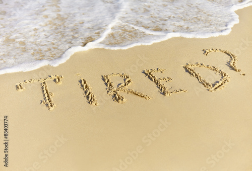 Tired written on the sand of the beach