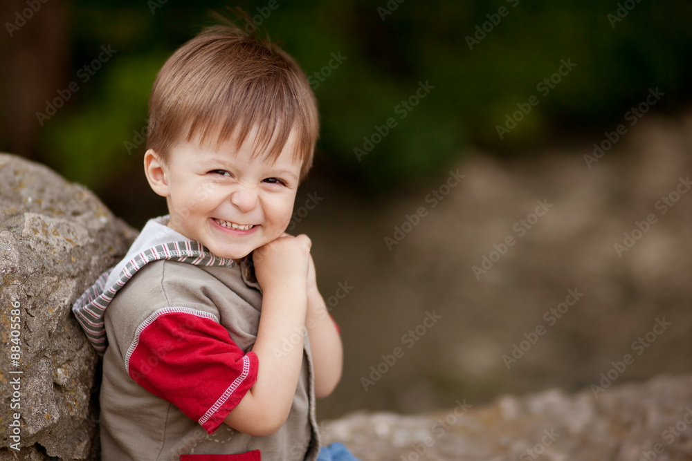 Portrait of happy little shy boy sitting on a stone with blank space on right Portrait of happy little shy boy sitting on a stone with blank space on right