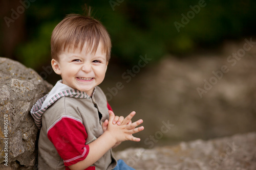 Portrait of happy little shy boy sitting on a stone with blank space on right