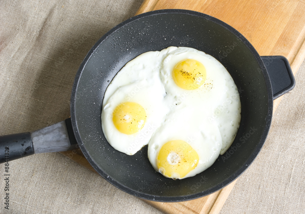 Three fried eggs in a pan on a wooden board and gray sackcloth Three fried eggs in a pan on a wooden board and gray sackcloth