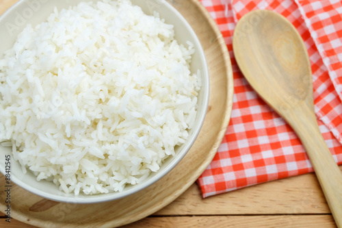 bowl full of rice in plate and spoon on wood