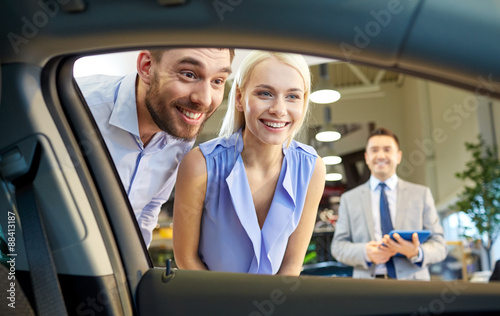 happy couple with car dealer in auto show or salon