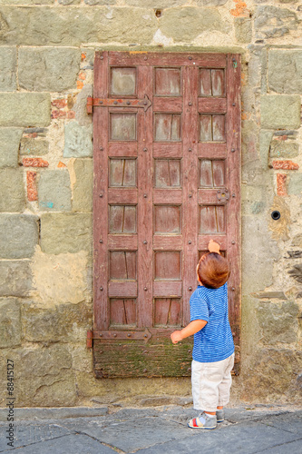 Child knocks an old medieval door asking reception