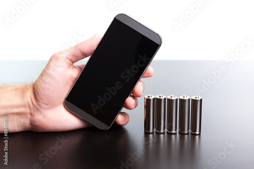 Man is holding a phone in his hand, and on the table are the batteries.