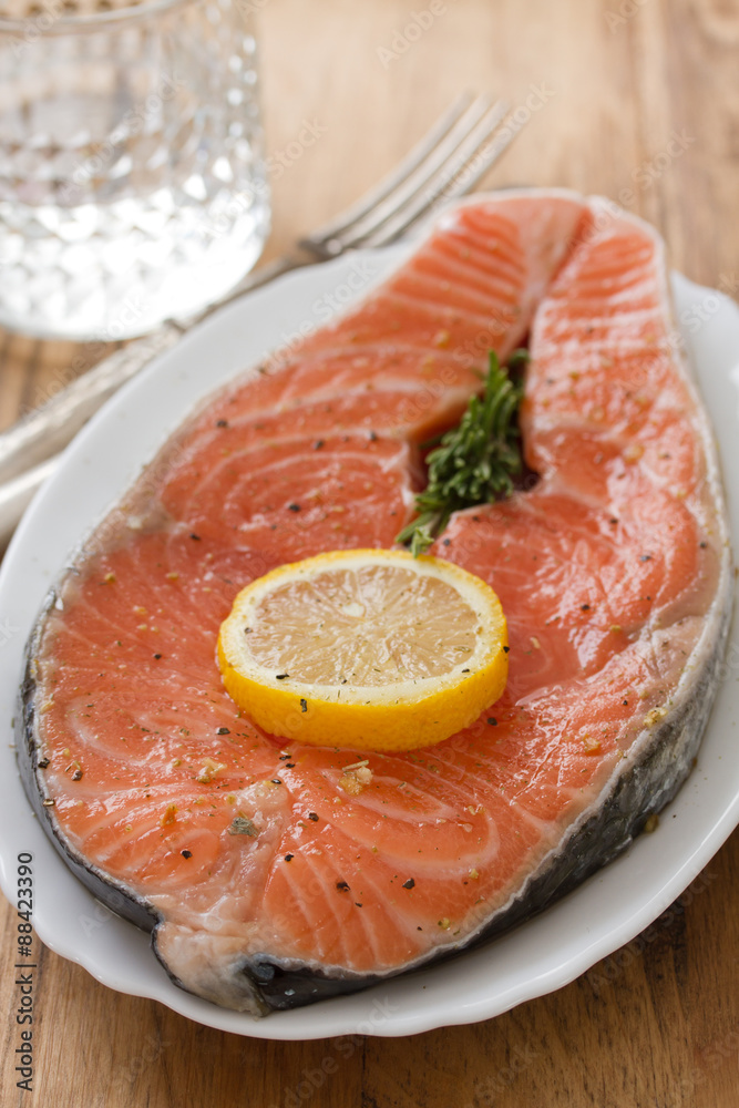 fresh salmon with lemon on white dish and glass of water on brown wooden background