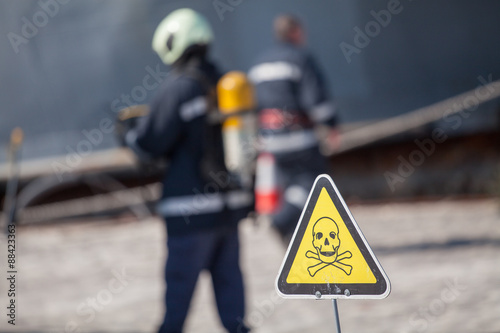 danger sign with skull and crossbones, firefighters on background © dechevm