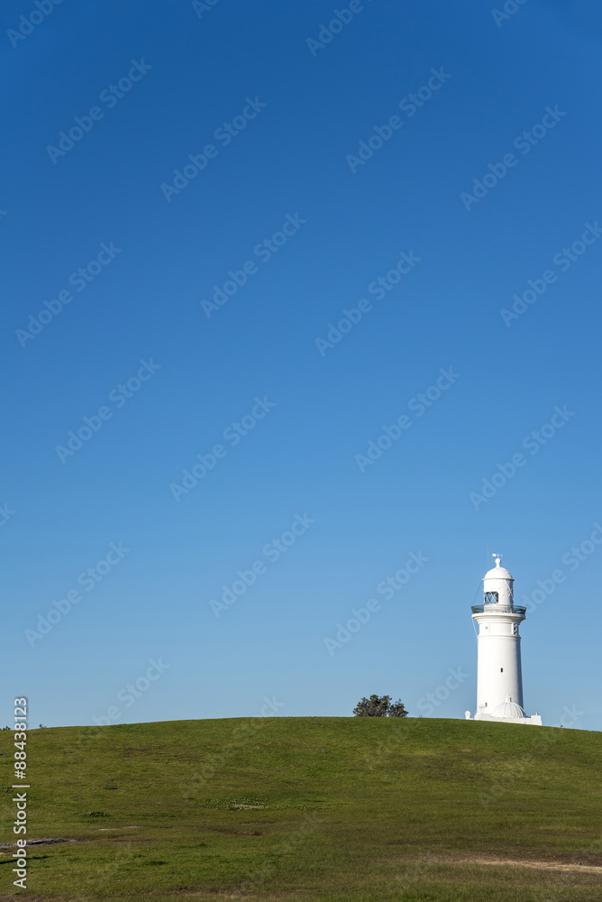 Macquarie Lighthouse on the horizon with green field and blue sky