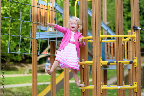 Happy kid enjoying active summer vacation. Adorable little child, blond cute toddler girl, having fun outdoors climbing on playground in the park on a sunny day © cromary